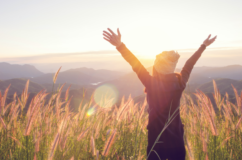 a woman with arms raised above overlooking valley at sunset to signify freedom experienced with therapy